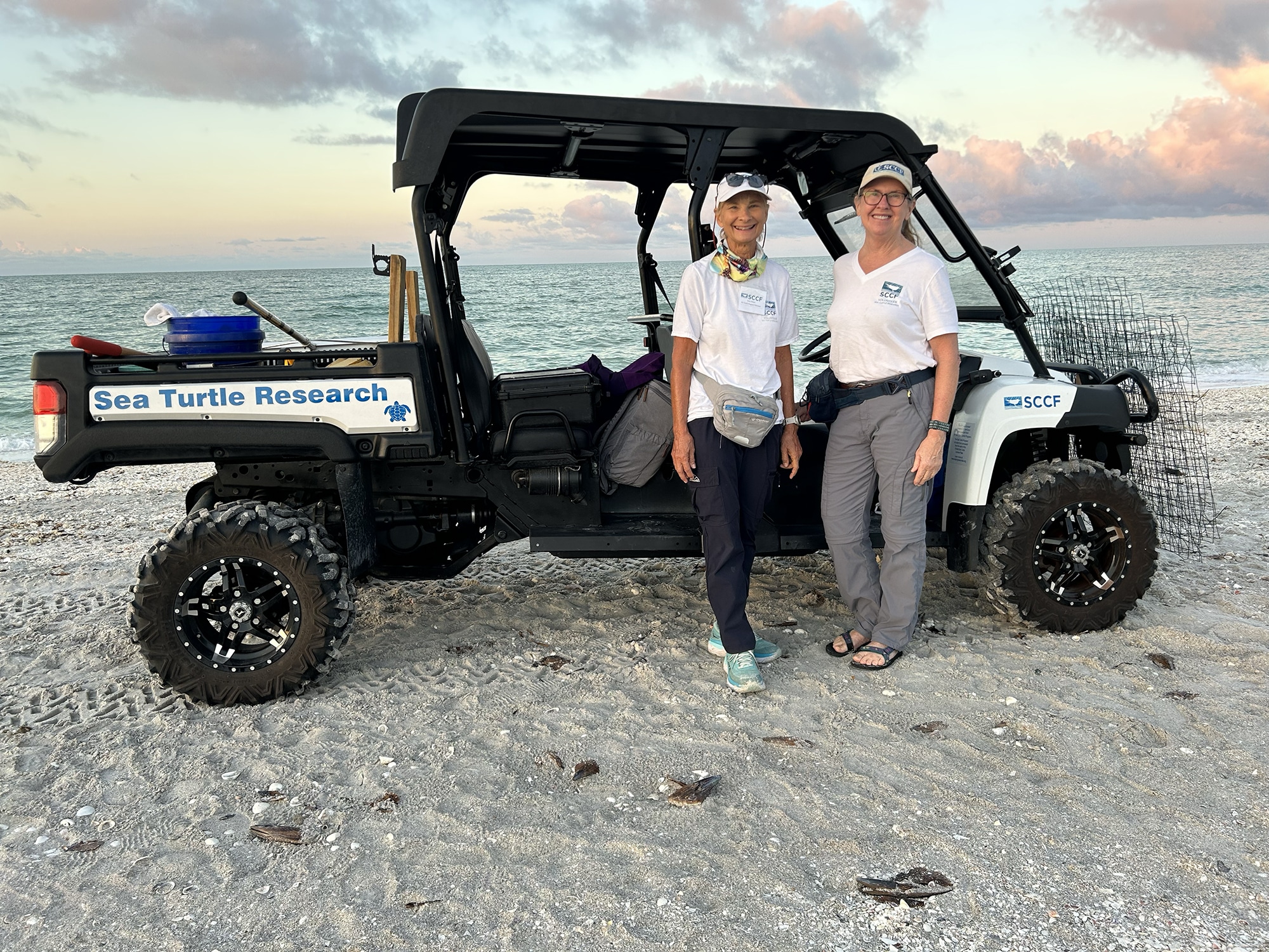 two women standing on beach in front of ATV