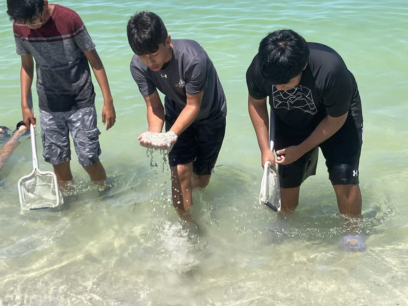 three kids sifting through sand on the beach