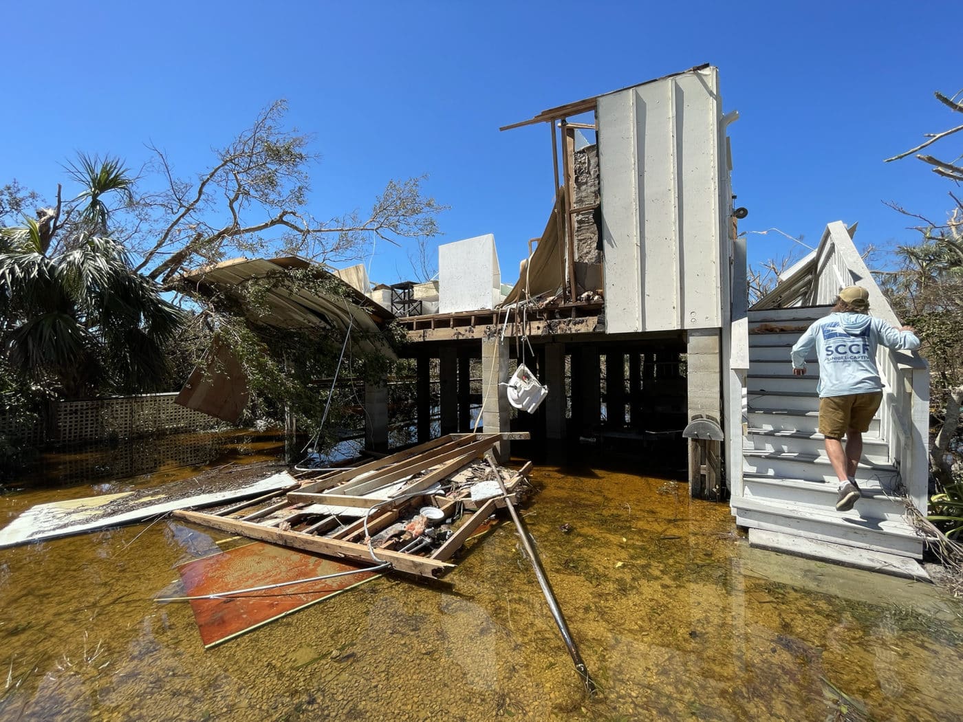 person walking into completely destroyed building with flood water surrounding it
