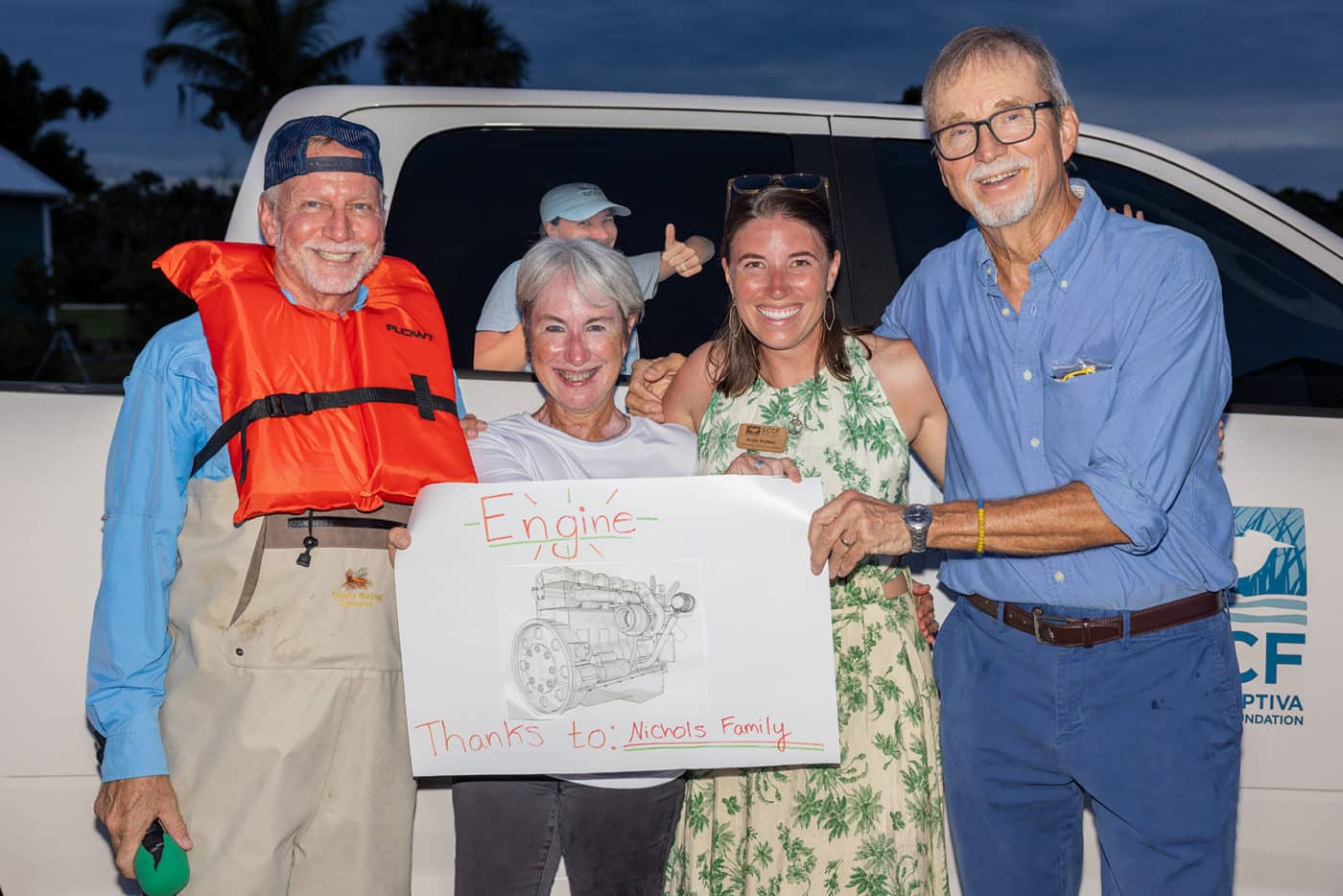 four people stand at watch party in front of a truck