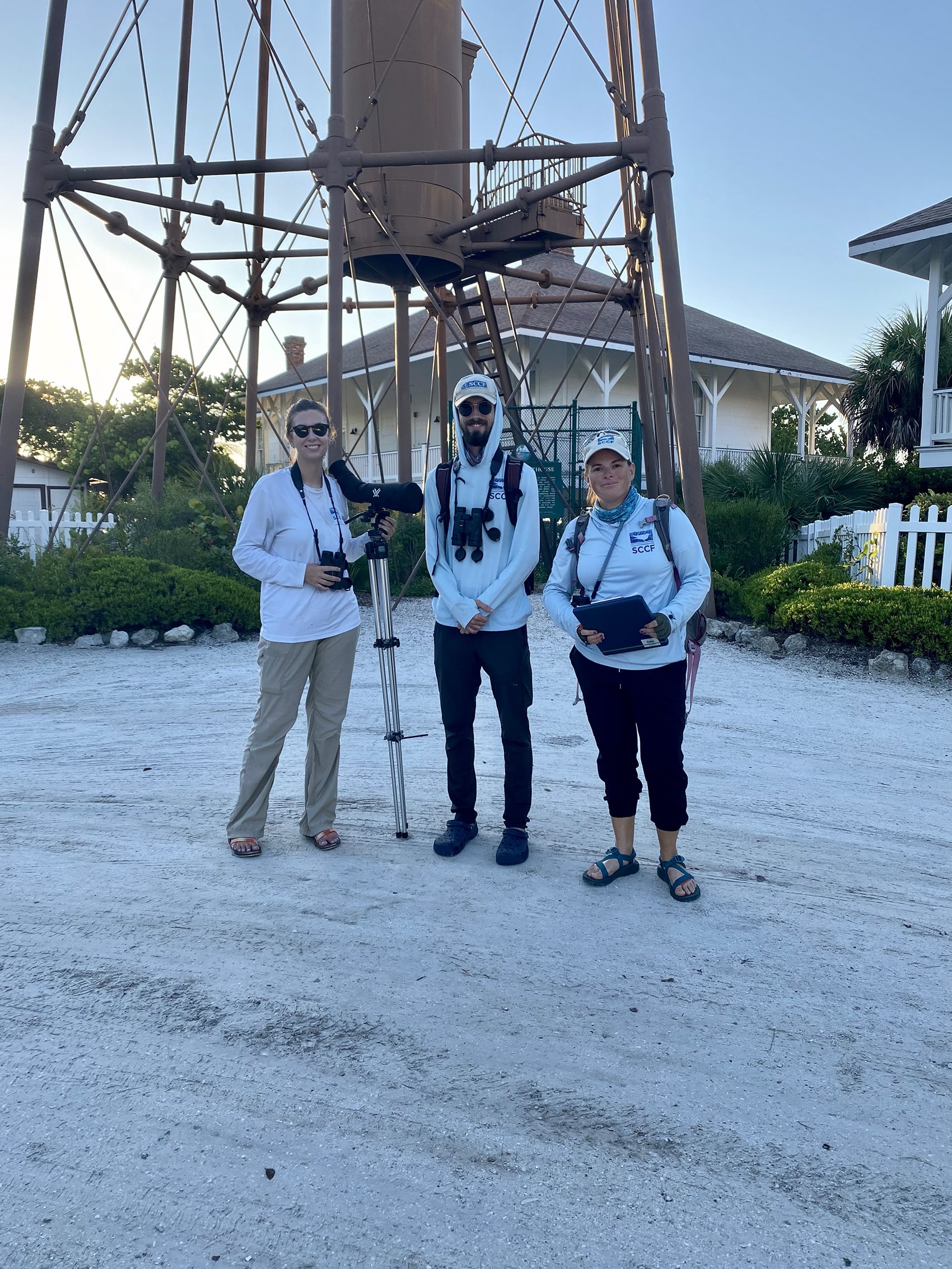 three sccf staff with binoculars in front of a lighthouse