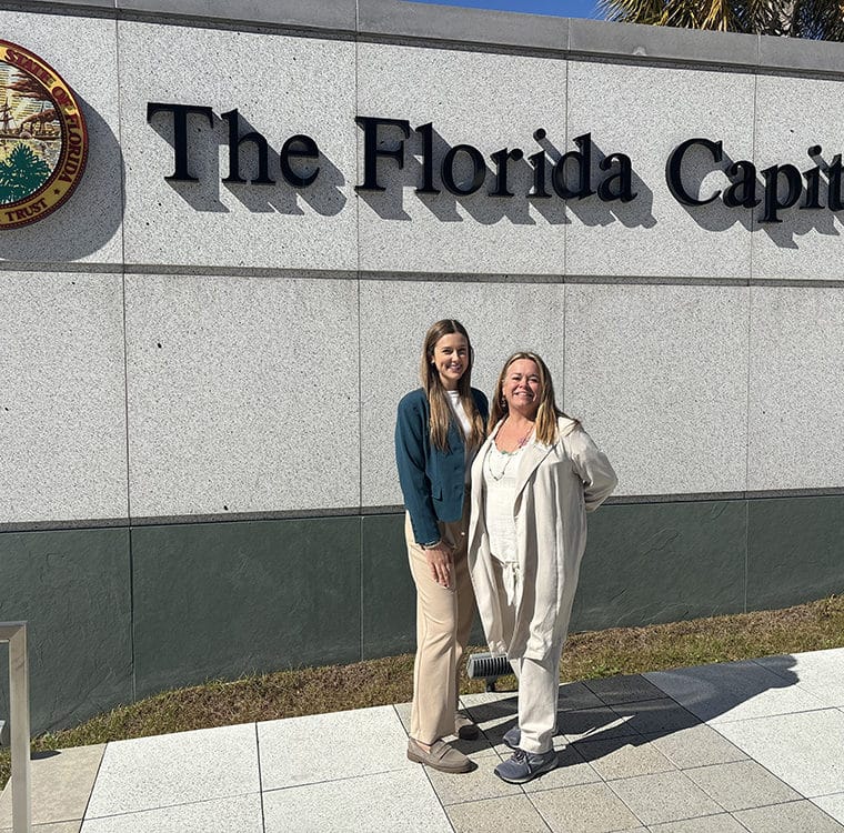 two women in front of outdoor sign that says 'the florida capitol'