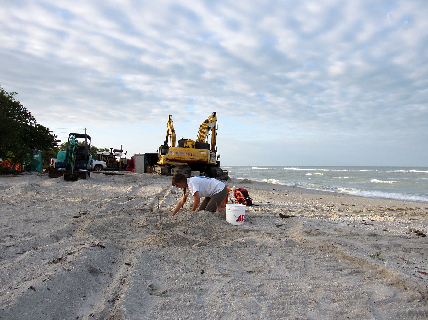 someone digging on beach in front of construction