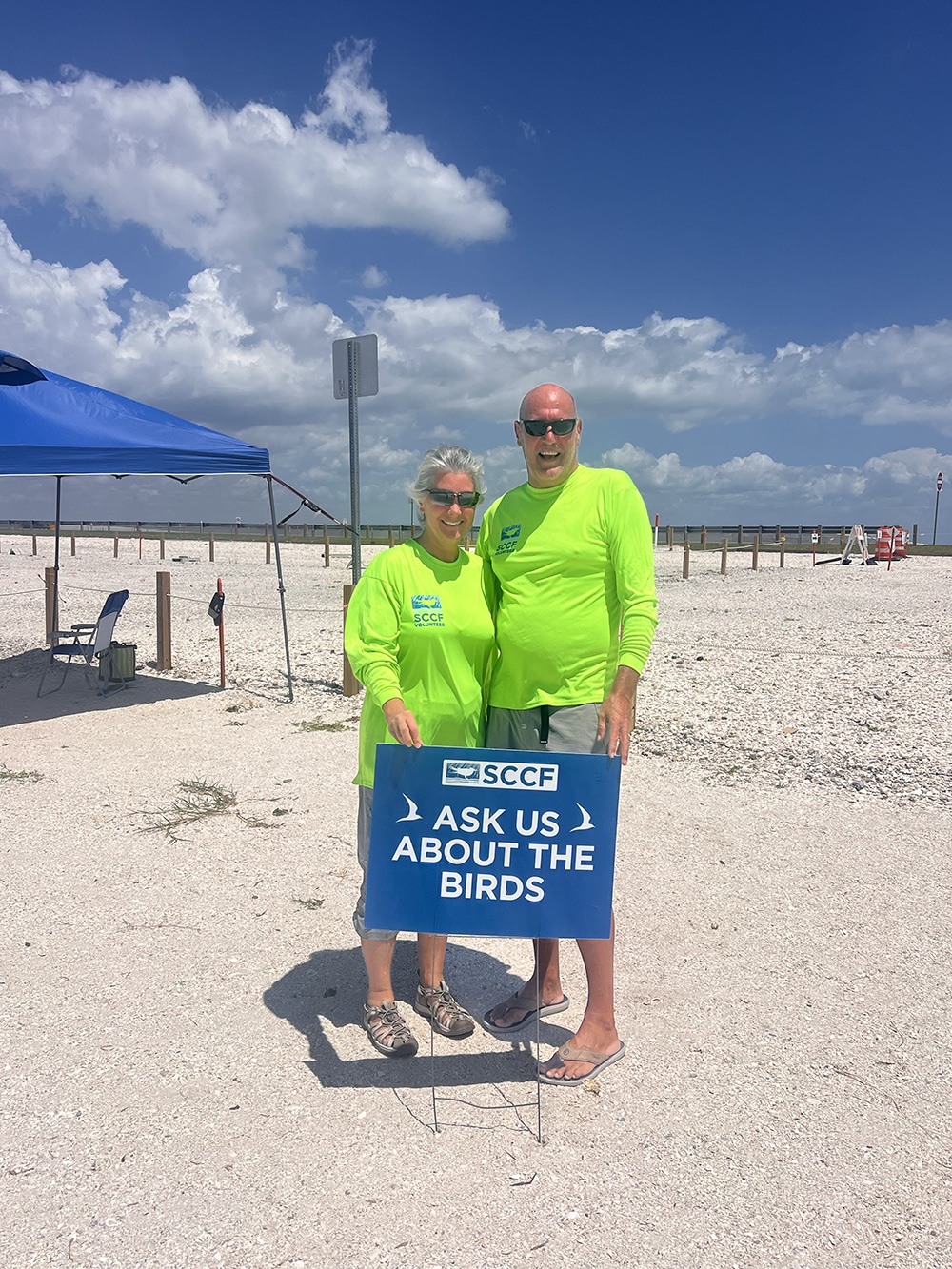 two shorebird volunteers standing in front of least tern nesting colony on sanibel causeway with sign that says "ask us about the birds"